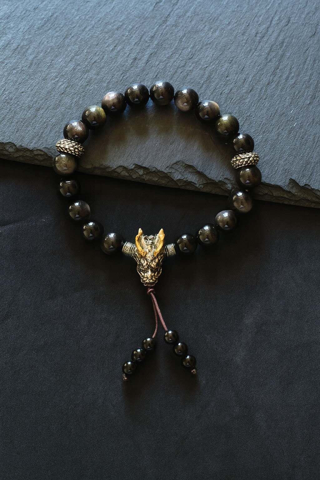 Bracelet with black beads and a dragon-shaped pendant on a dark surface