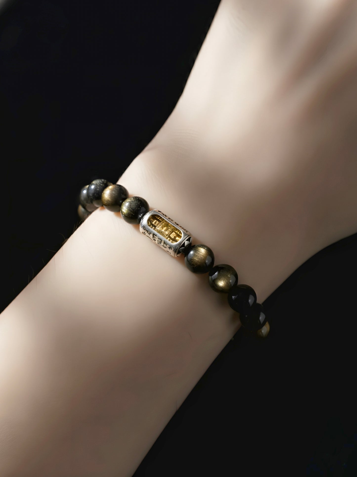 Bracelet with dark beads and a gold clasp on a wrist against a black background