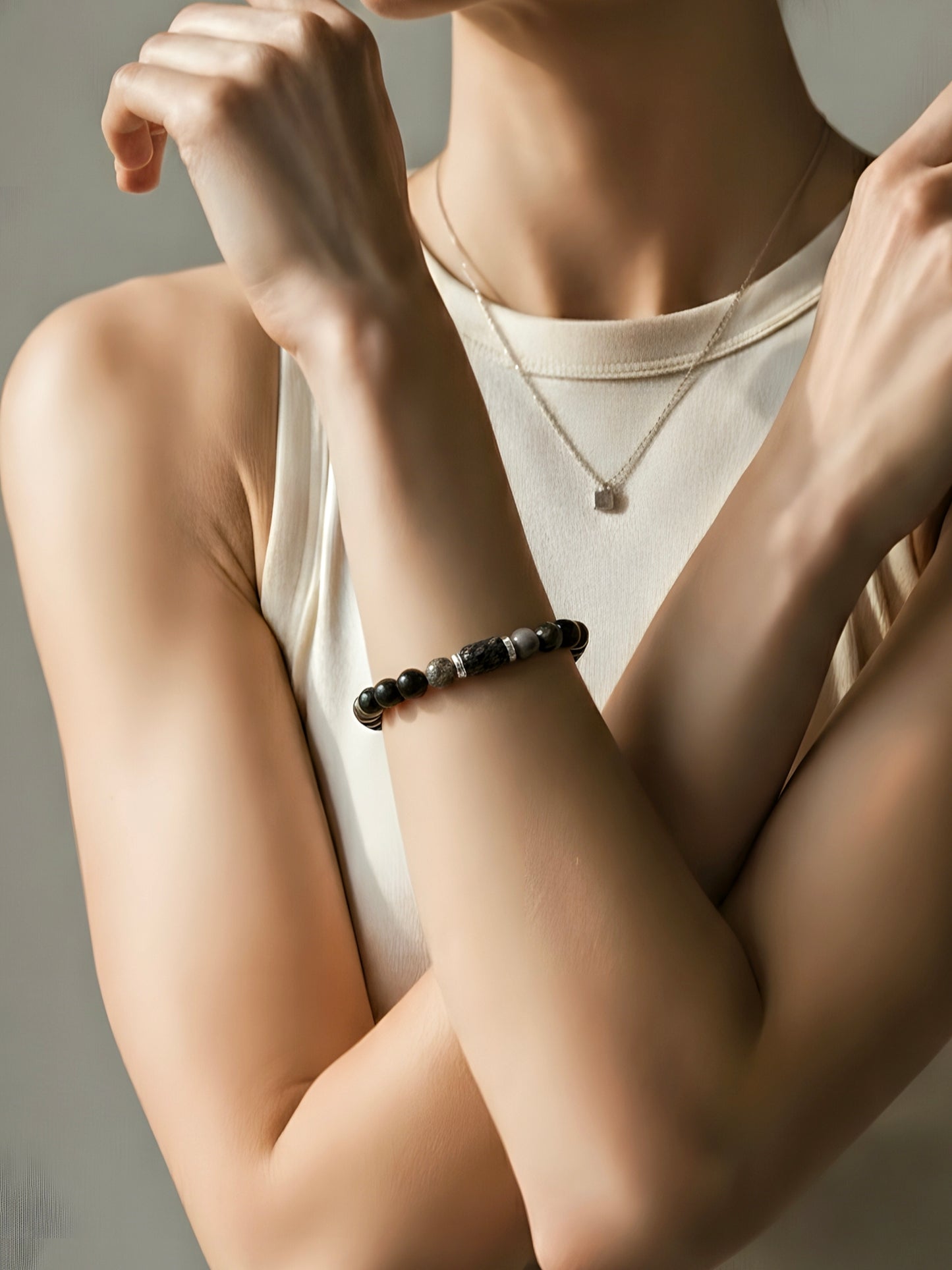 Person wearing a necklace and bracelet on a neutral background