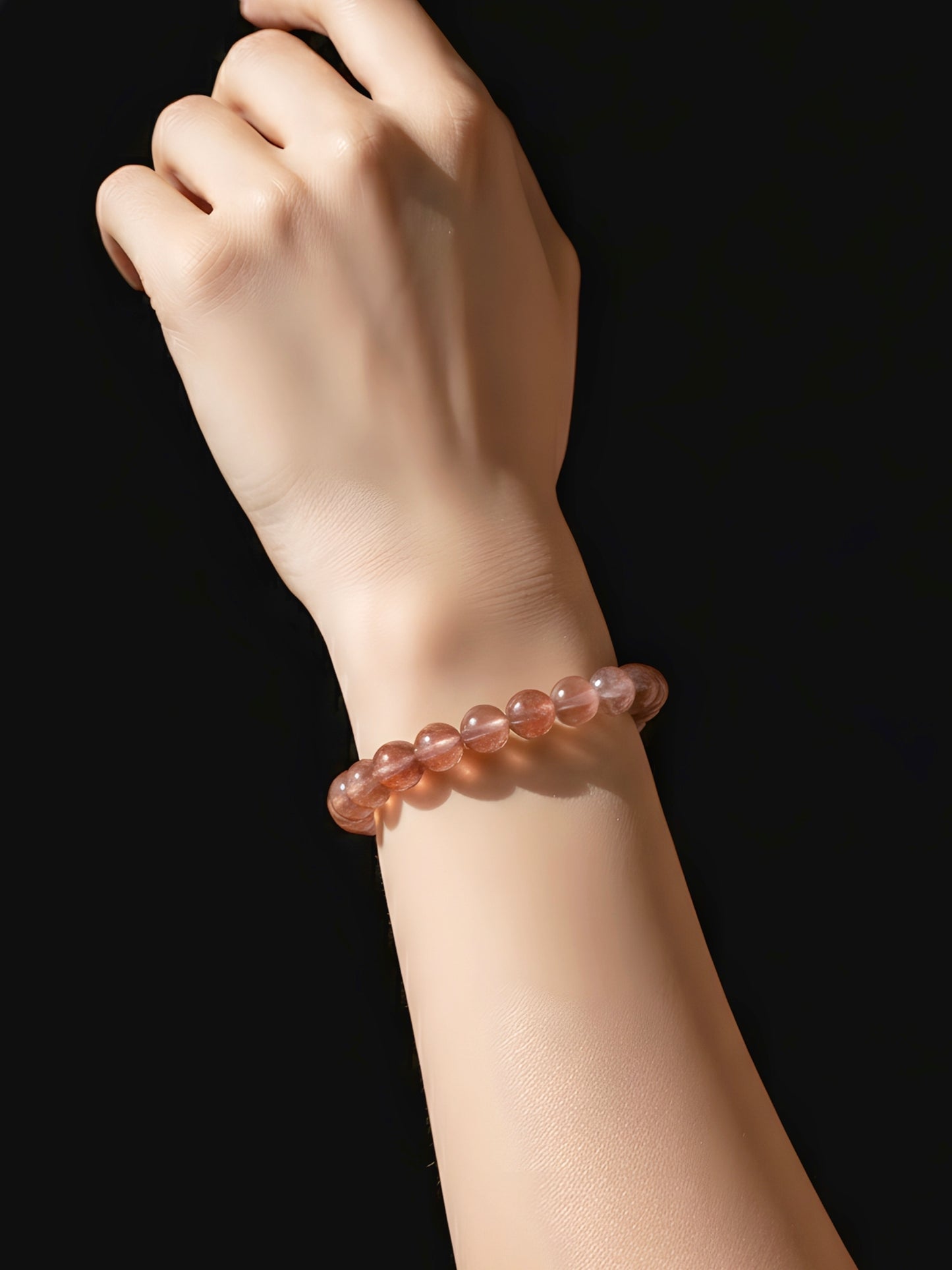 Hand wearing a pink beaded bracelet on a black background