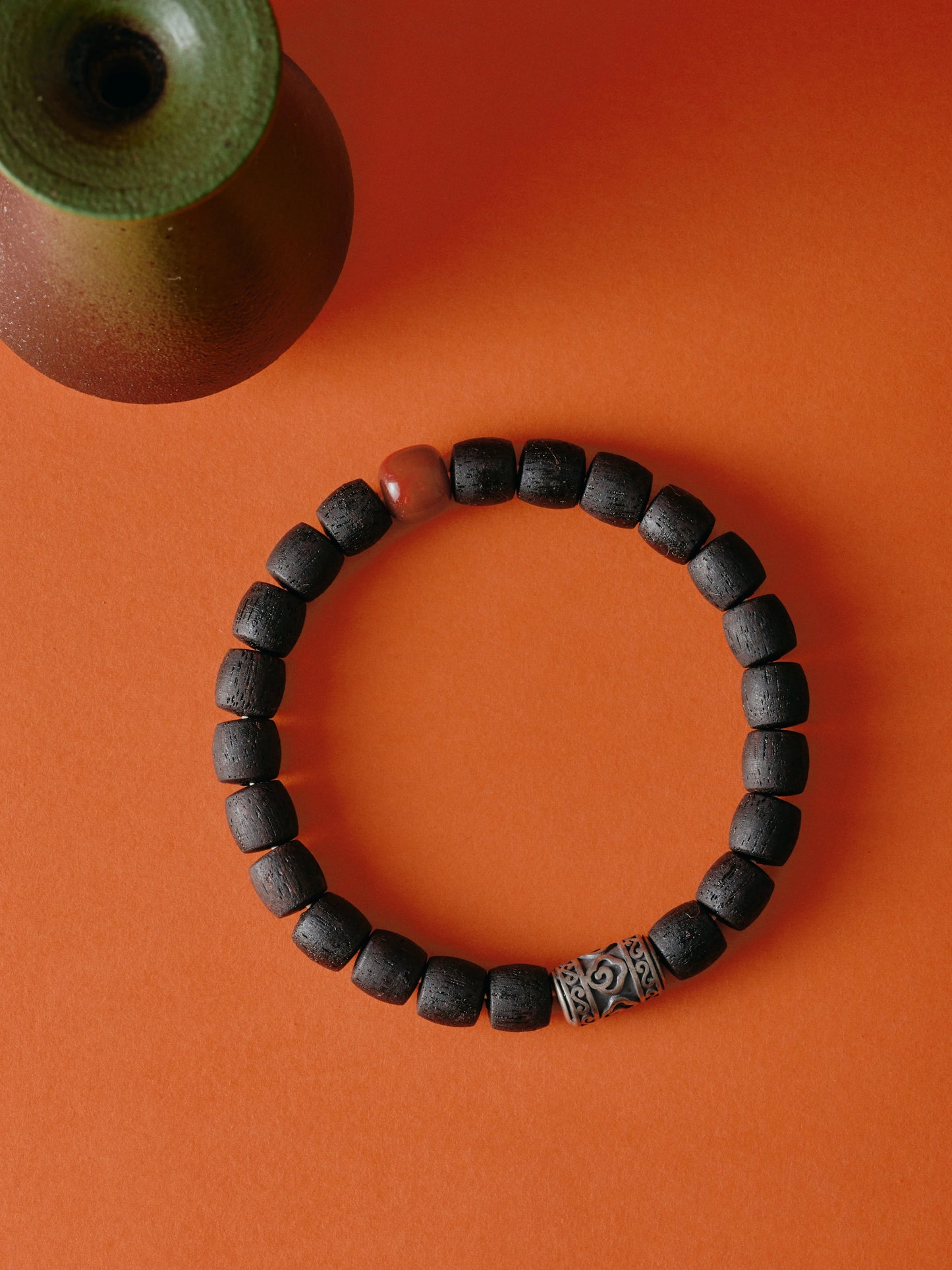 Black beaded bracelet with a silver clasp on an orange background