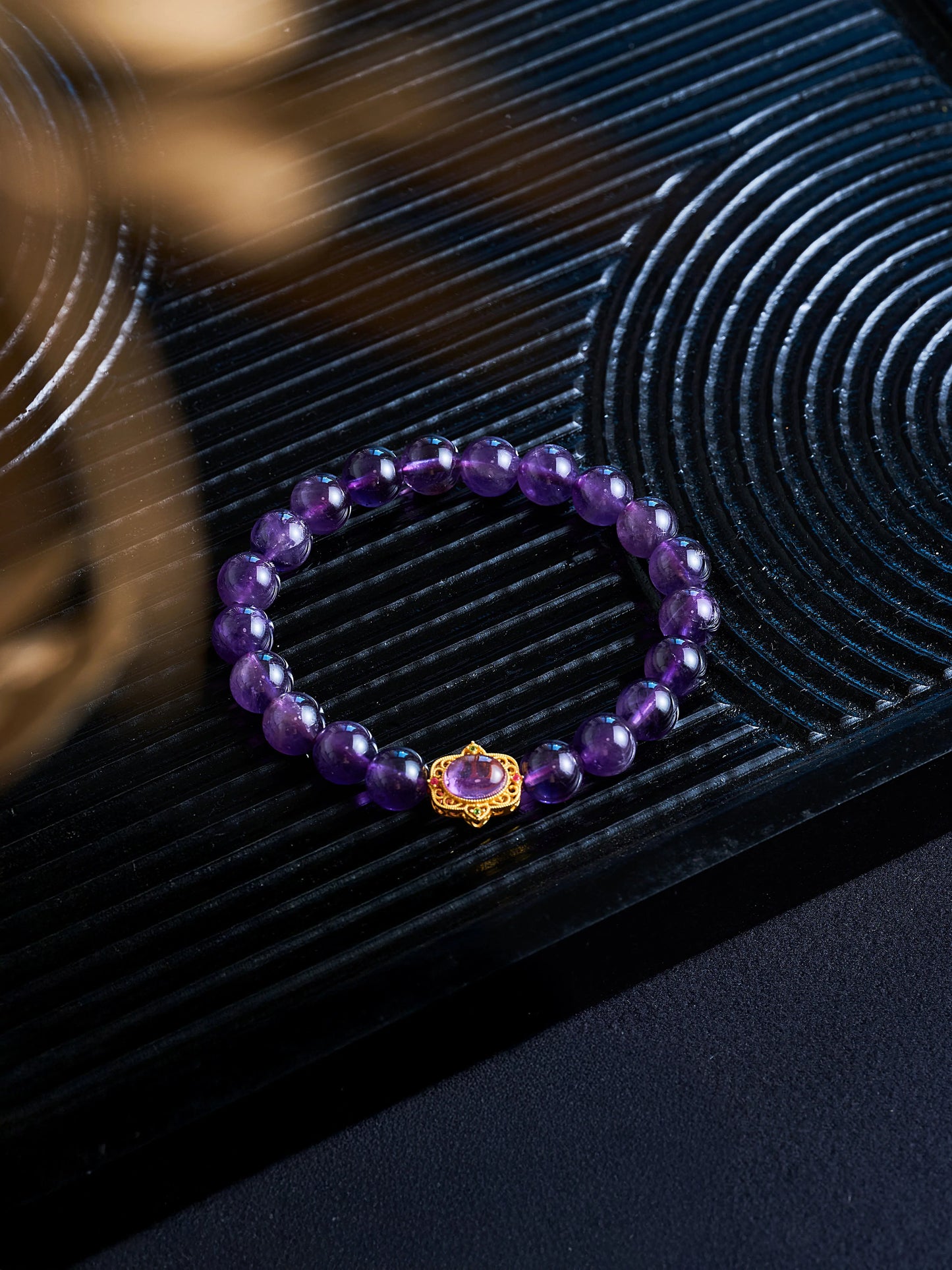 Purple beaded bracelet with a gold clasp on a textured black surface