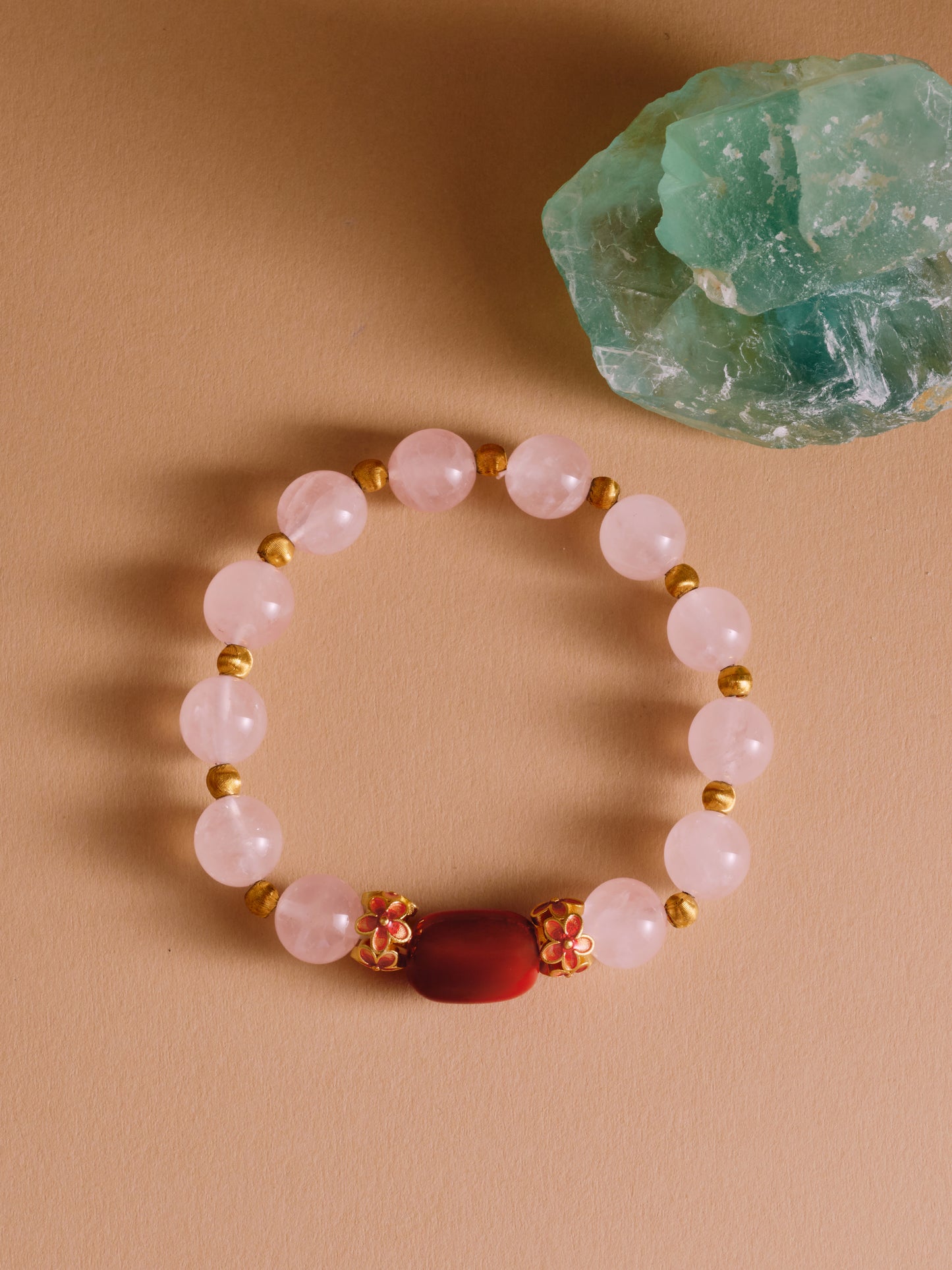 Beaded bracelet with gold accents on a beige surface next to a green crystal.