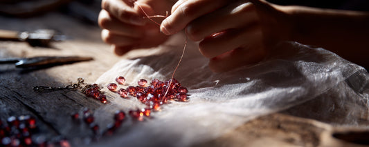 Hands restringing collected round crystal beads from a broken bracelet into a new necklace.