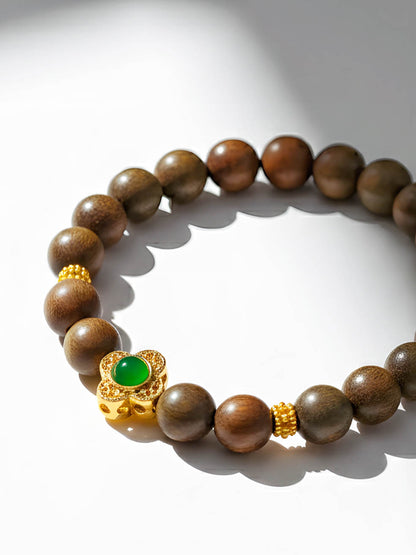 Wooden beaded bracelet with a gold clasp and green gemstone on a white background