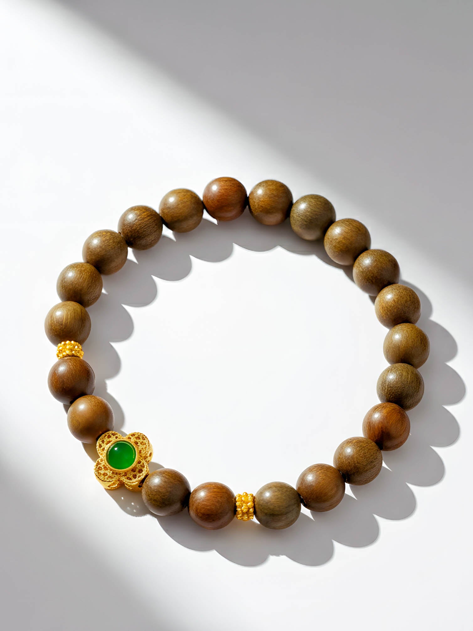 Wooden beaded bracelet with a gold clasp and green gemstone on a white background