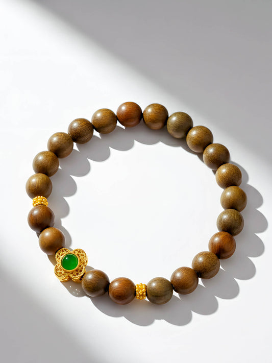 Wooden beaded bracelet with a gold clasp and green gemstone on a white background