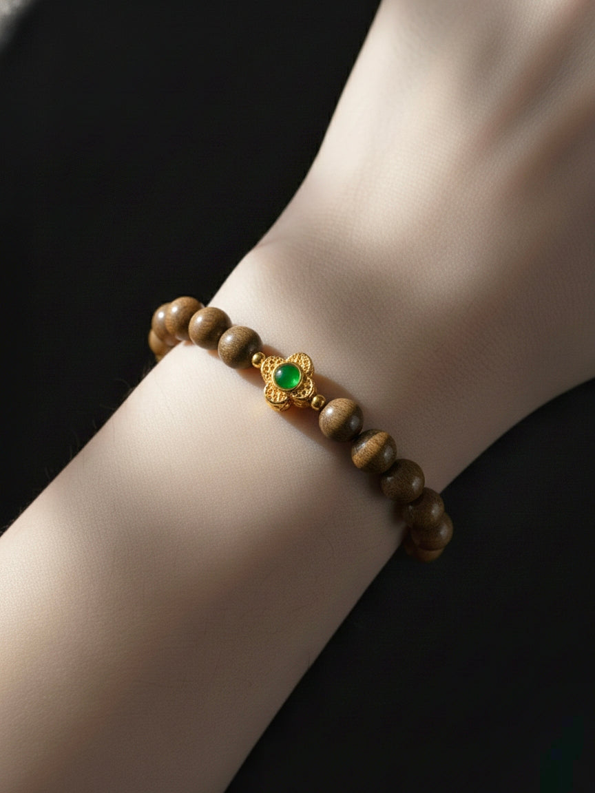 Bracelet with wooden beads and a green gemstone on a wrist against a black background