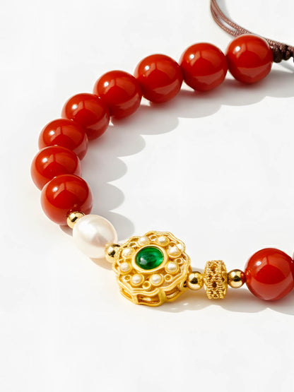 Bracelet with red beads, gold clasp, and green gemstone on a white background