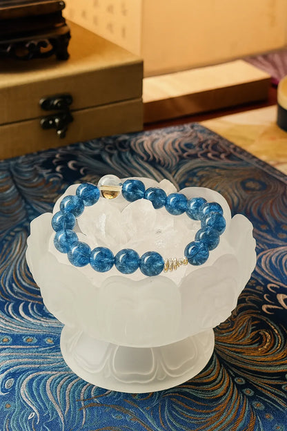 Blue beaded bracelet on a white pedestal against a decorative blue and gold background