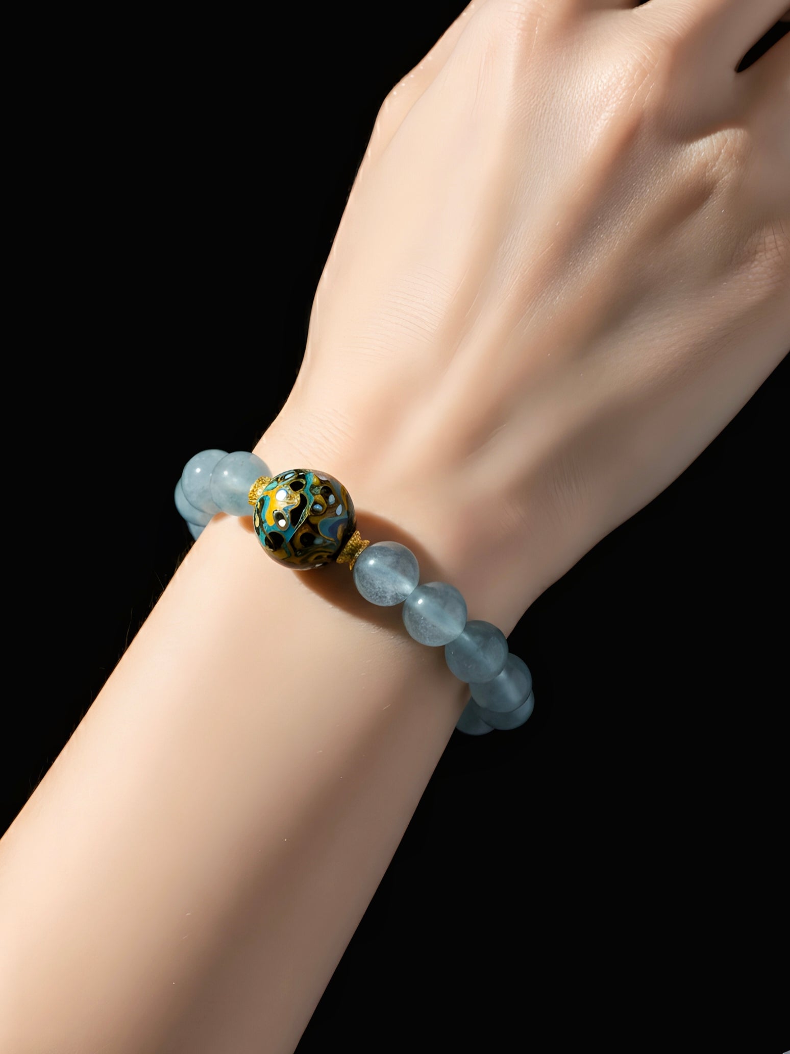 Hand wearing a bracelet with a dark green bead on a black background