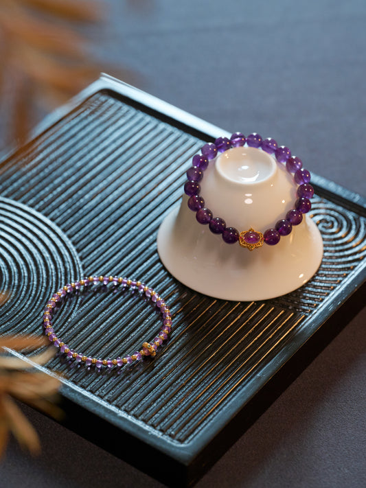 Two purple beaded bracelets on a small white stand with a blurred background
