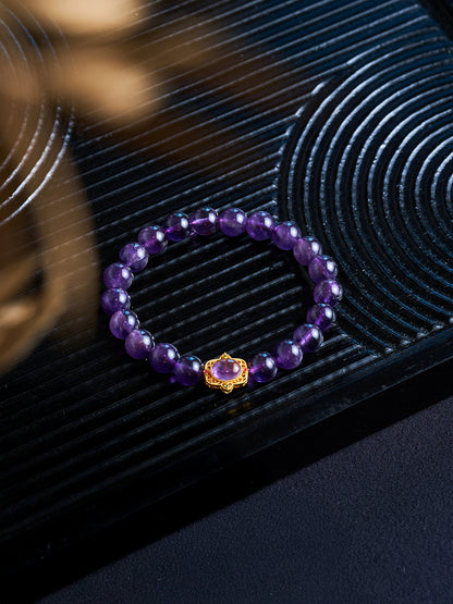 Purple beaded bracelet with a gold clasp on a textured black surface