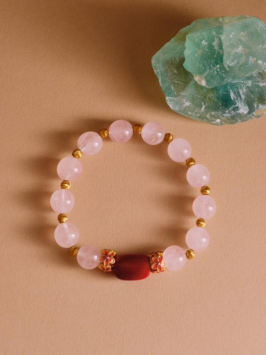 Beaded bracelet with gold accents on a beige surface next to a green crystal.